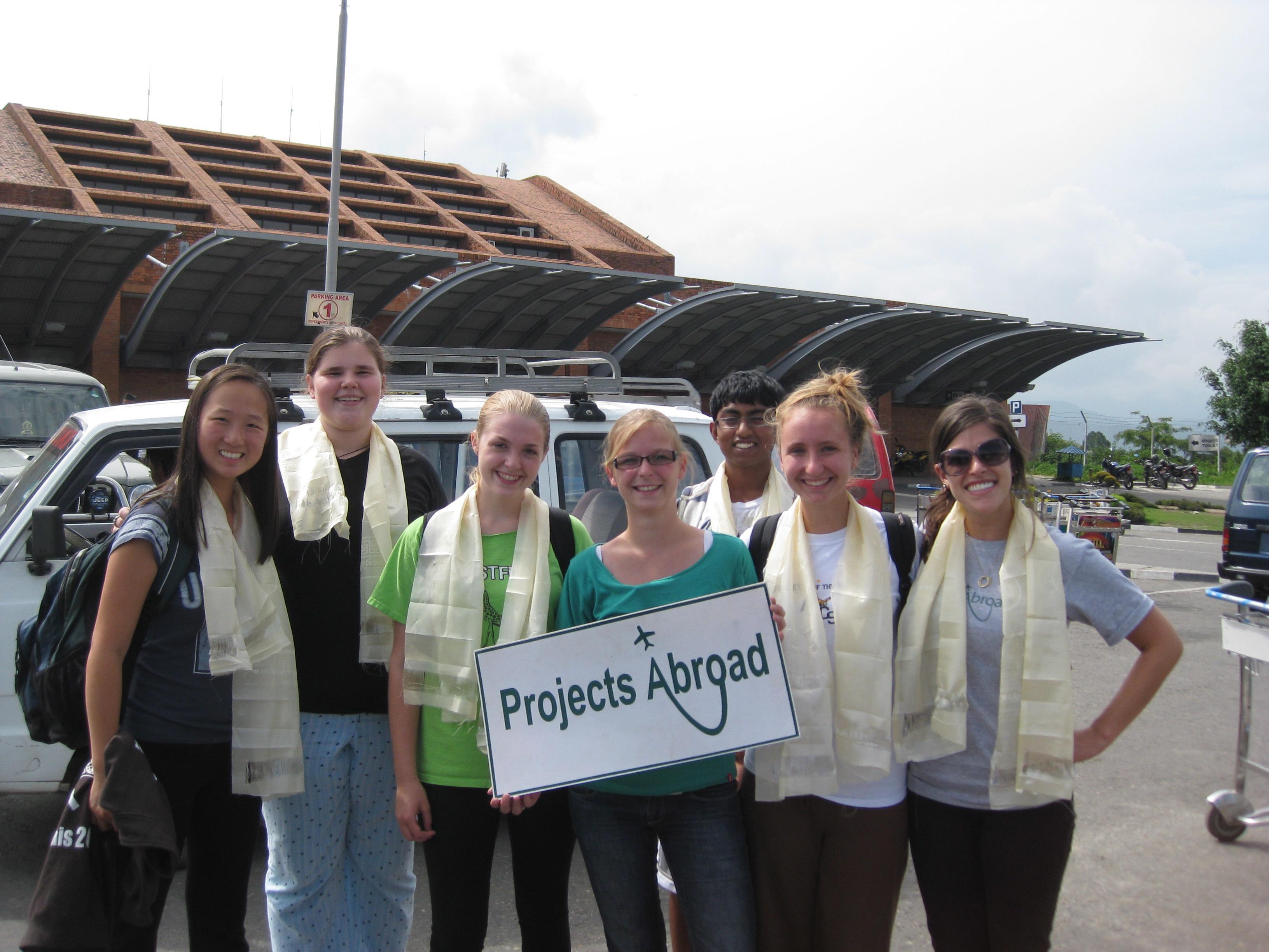 Volunteers stand with the Projects Abroad sign and staff in Nepal Volunteers get picked up at the airport by Projects Abroad staff after arriving in Nepal