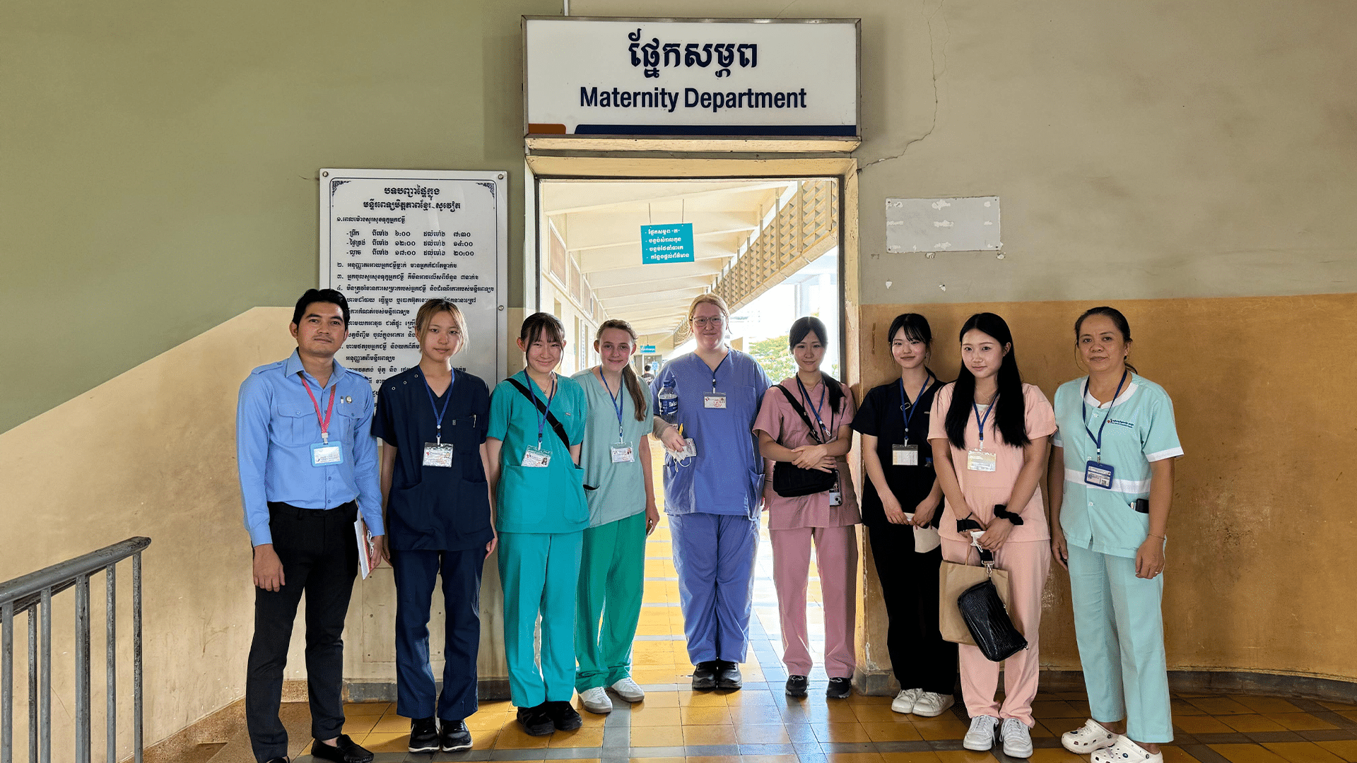 A group of nine medical interns and staff stand in a row under a sign that reads "Maternity Department" in English and Khmer.